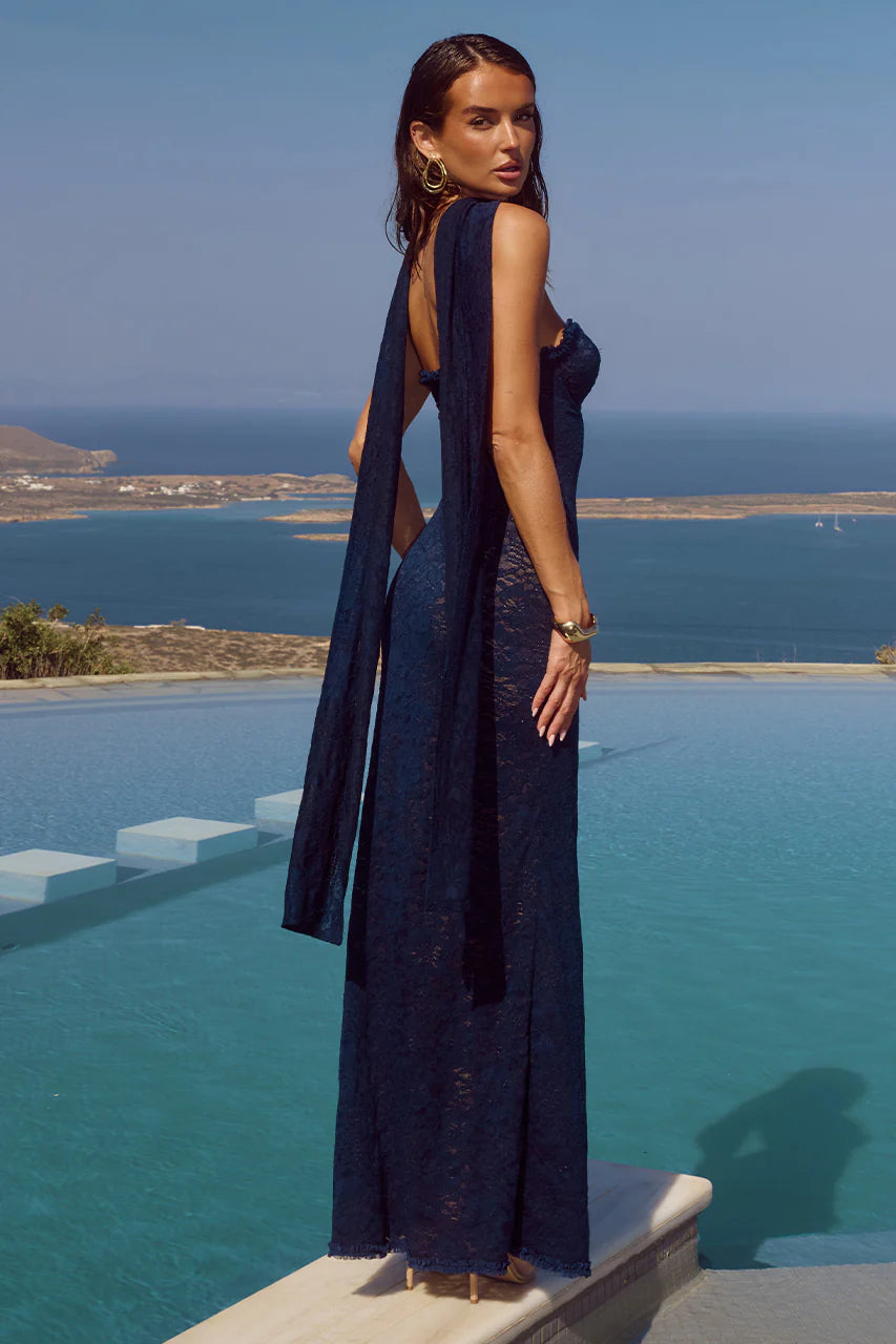 Woman in a navy blue dress standing by an infinity pool with a scenic view of the ocean.
