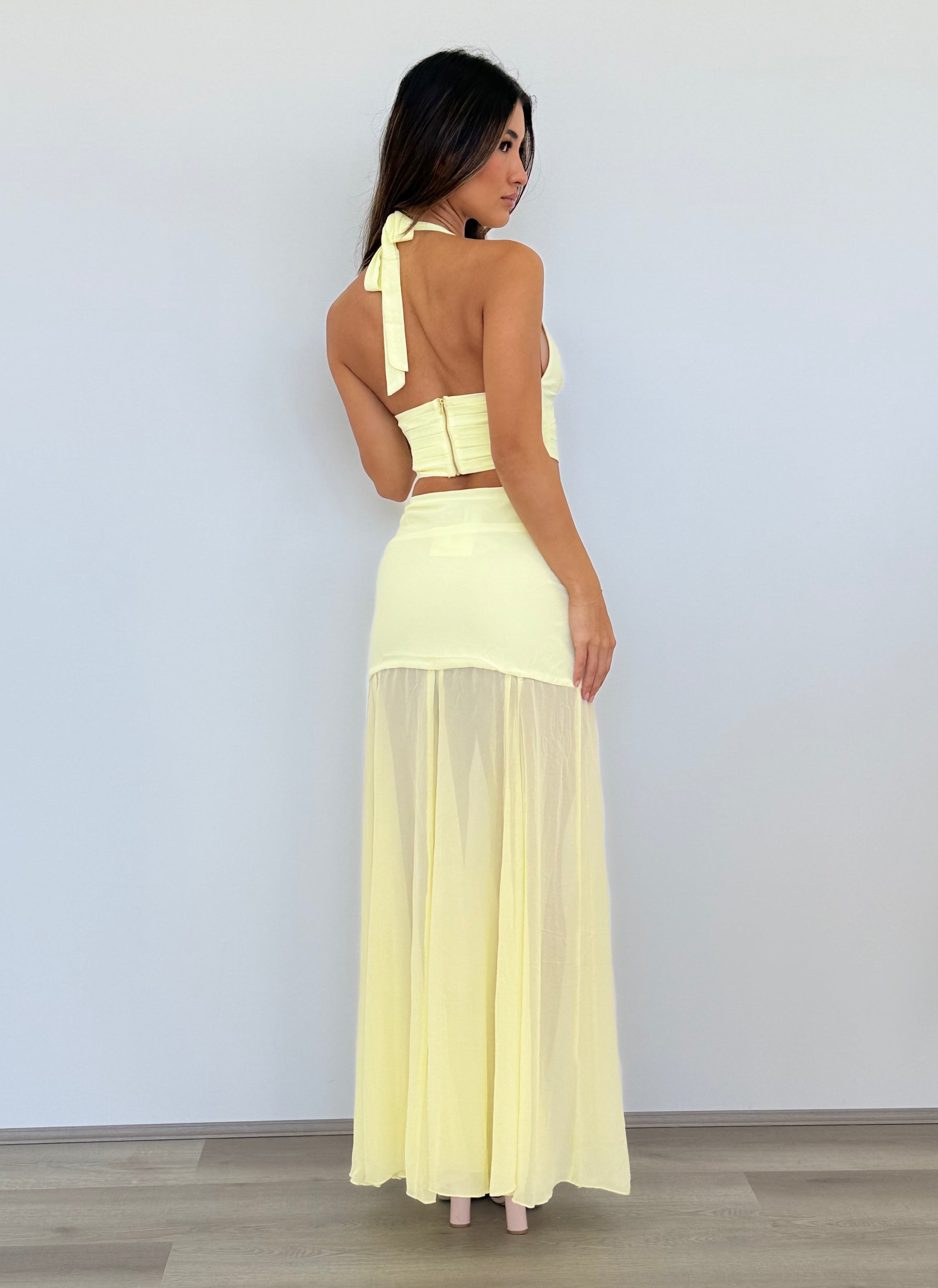 Woman wearing a light yellow dress standing against a white wall.