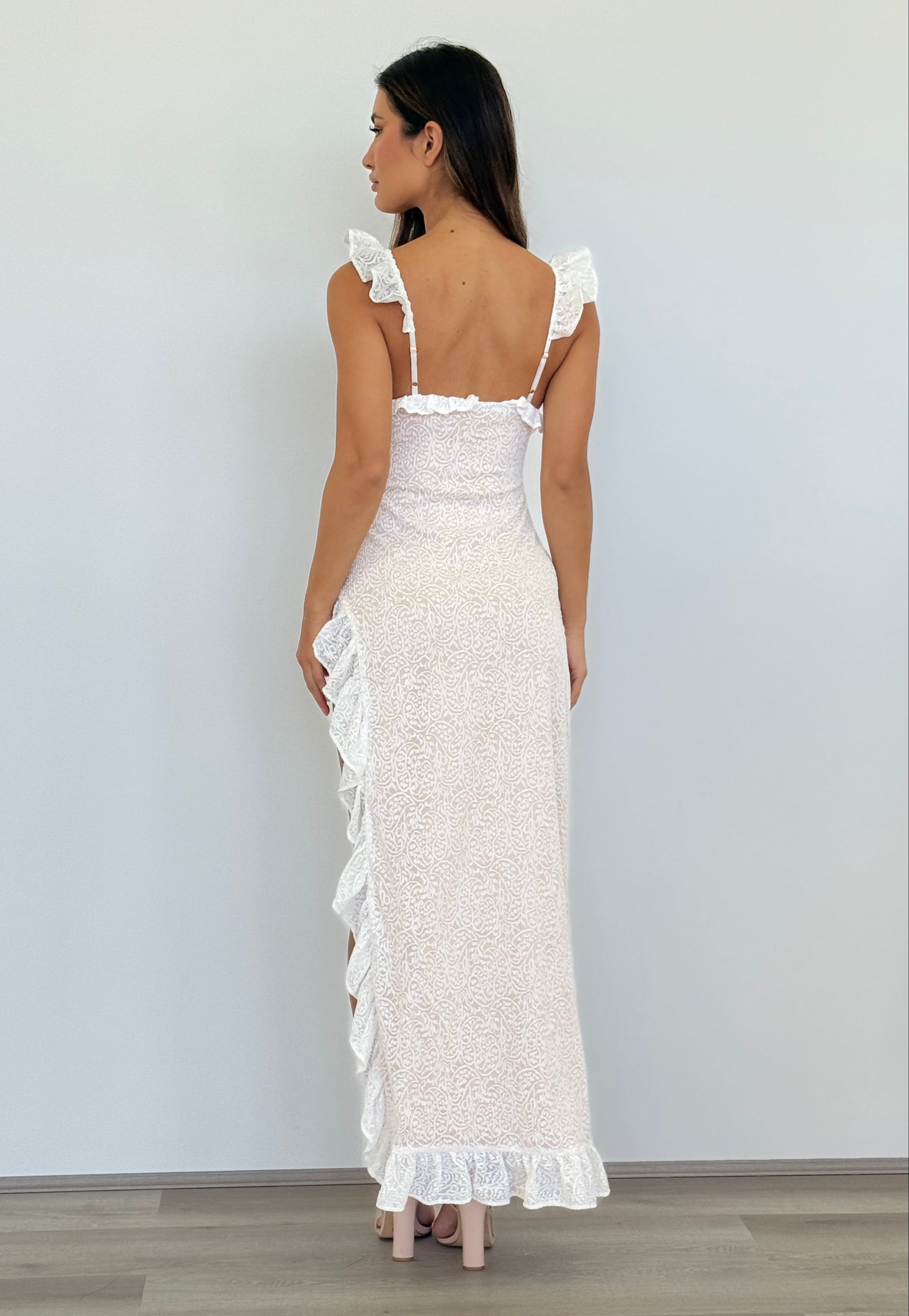 Woman wearing a white lace dress with ruffled details, standing against a plain background.