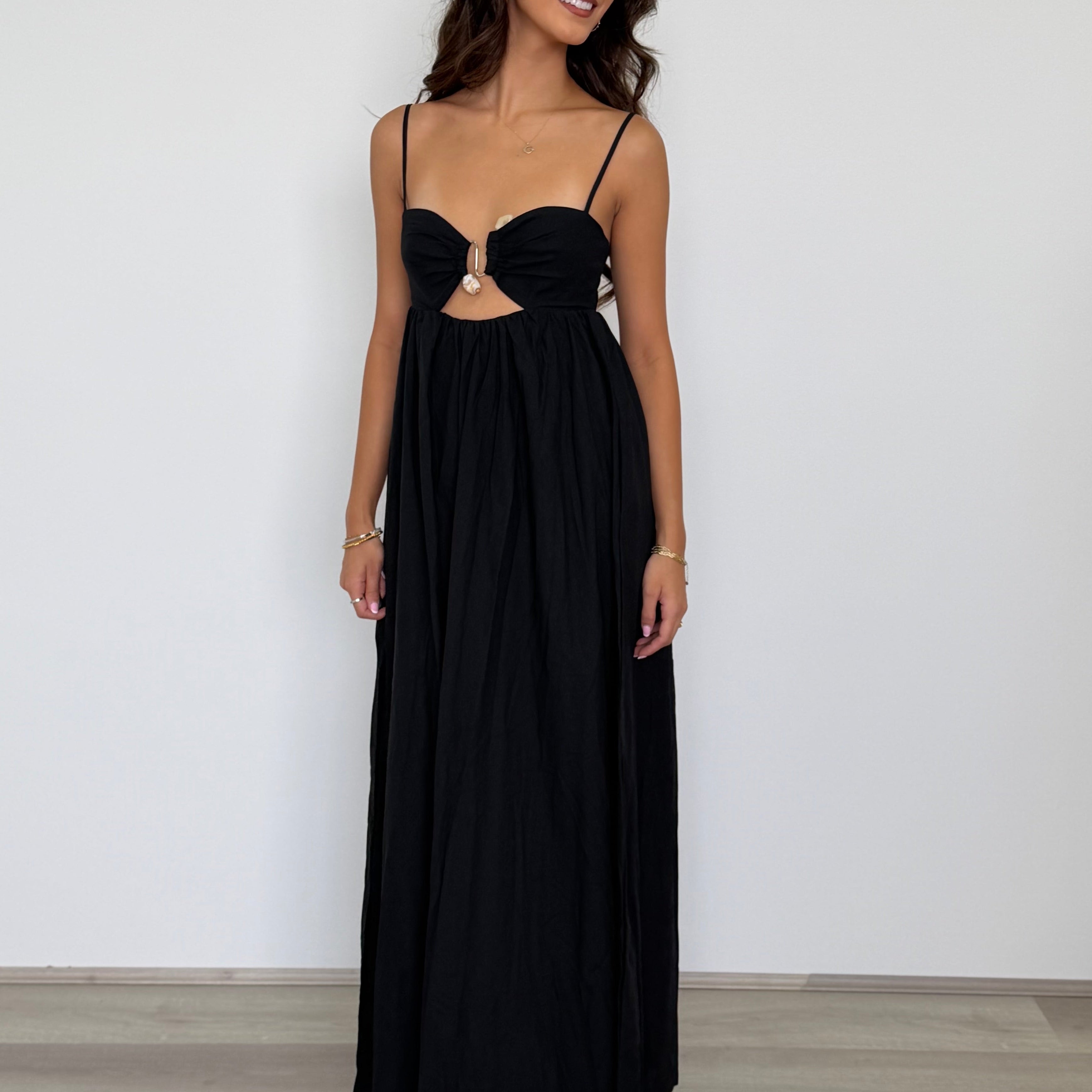 Woman wearing a black evening gown with cut-out design against a plain background
