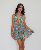 Woman wearing a colorful paisley dress against a plain background