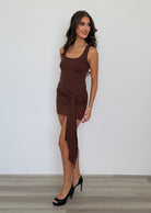 Woman wearing a brown dress standing against a white wall.