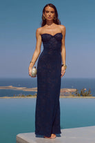 Woman in a strapless navy blue gown standing by a pool with a scenic background