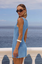 Woman in a blue dress with cut-out design standing by the ocean.