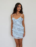 Woman wearing a light blue ruffled dress against a plain background