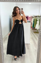 Woman in a black dress taking a mirror selfie in a store.