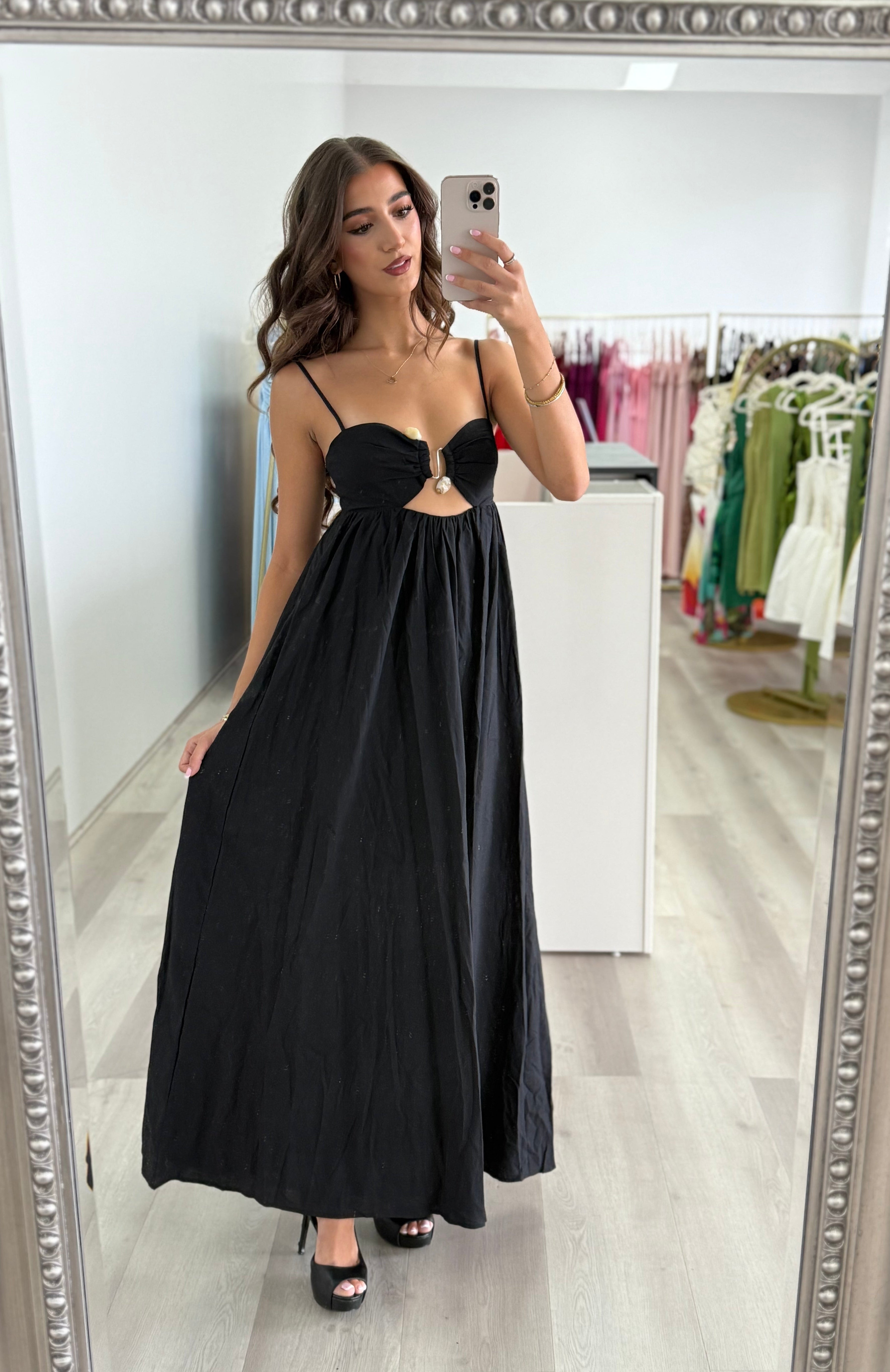 Woman in a black dress taking a mirror selfie in a store.