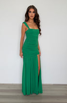 Woman wearing a green dress with a slit on a plain background