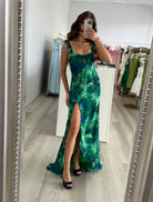 Woman in a green and blue patterned dress standing in front of a mirror a clothing shop.