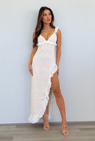 Woman wearing a white lace dress with a high slit against a plain background