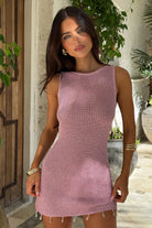 Woman wearing a pink knitted dress standing outdoors with plants in the background
